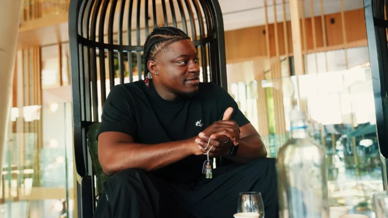 Jonge man met cornrows en amulet in een lichte omgeving.